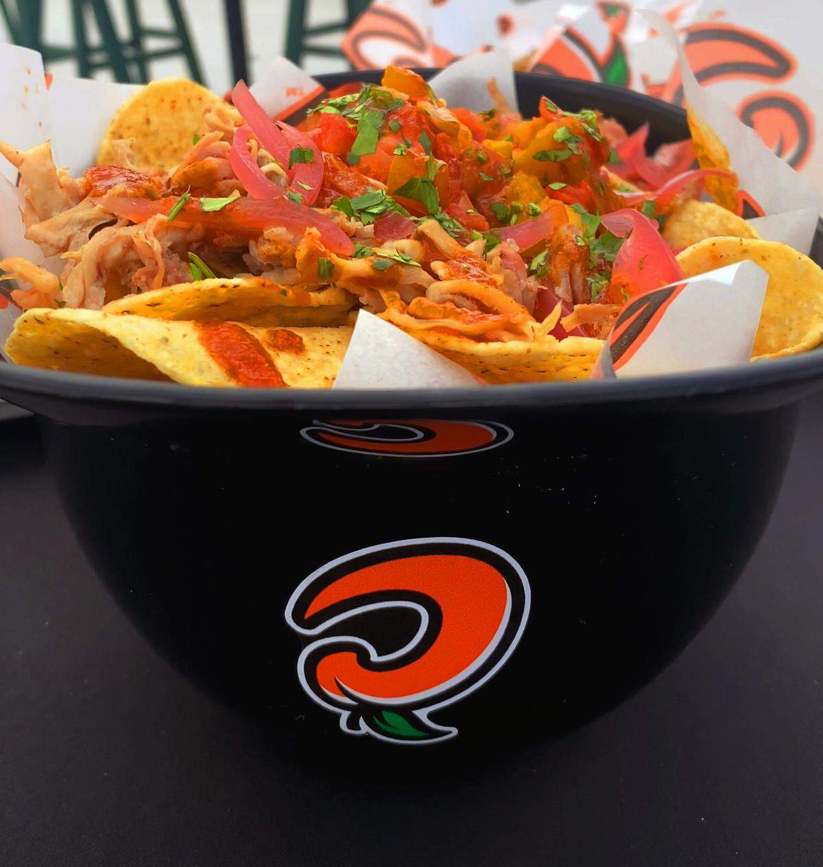 The loaded pulled-pork nachos feature queso blanco, pulled pork, a house-made peach barbecue sauce, and pickled red onions in a souvenir baseball helmet. 04/11/2025