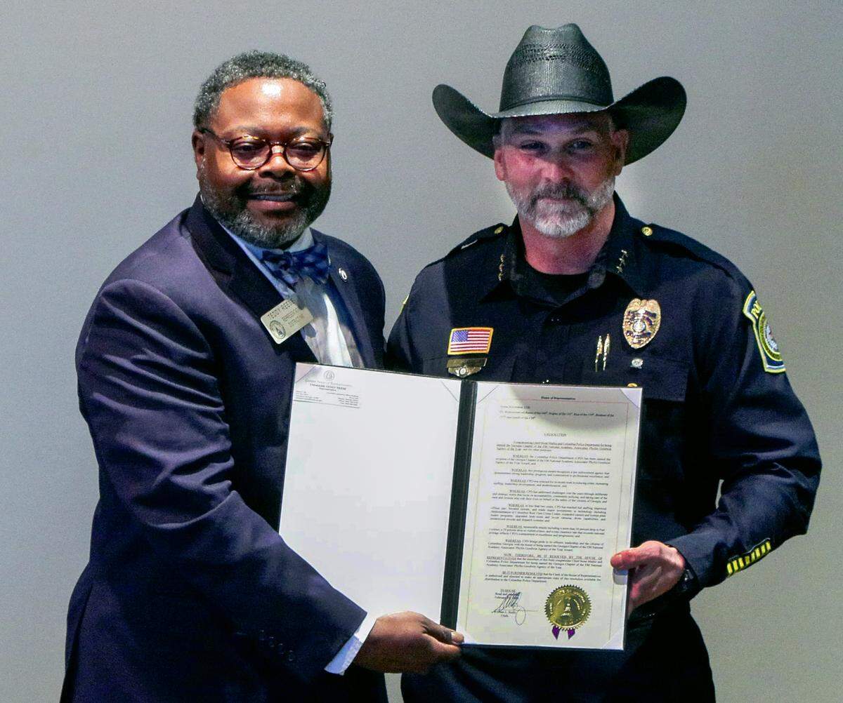 During an April 7, 2026, news conference at the Columbus Police Department headquarters, Georgia state Rep. Teddy Reese (D-Columbus), left, presents Lance Deaton, CPD assistant chief of operations, with a resolution congratulating Columbus Police Chief Stoney Mathis and CPD for being named the Georgia Chapter of the FBI National Academy Associates’ Phyllis Goodwin Agency of the Year.