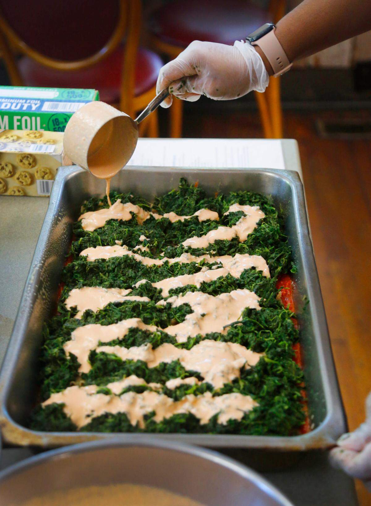 Terriann White, the kitchen supervisor at Country Life in Columbus, adds cashew cheese sauce to a pan of their vegan lasagna recipe. 05/05/2025