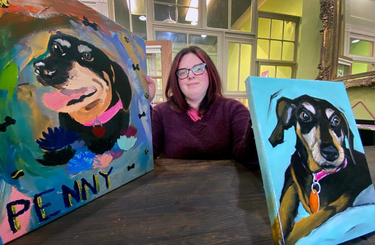 Loren Van Pelt holds paintings by local artists Kweisi Daniels, left, and Claire O’Connor, right, she was given of her dog Penny after Penny’s death. 02/24/2022