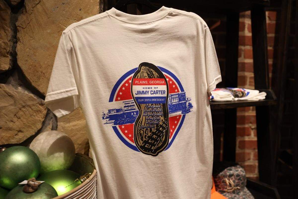 Jimmy Carter t-shirts hang in Plains Sweet Stems on Main Street in downtown Plains, Georgia on the evening of former president Jimmy Carter’s death on Sunday, Dec. 29, 2024, in Plains. The shop’s co-owner Jilliann Williams said she came to set up more shirts in the shop this evening after hearing of Carter’s death, and in preparation for those that will come into town over the next several days to pay respects.
