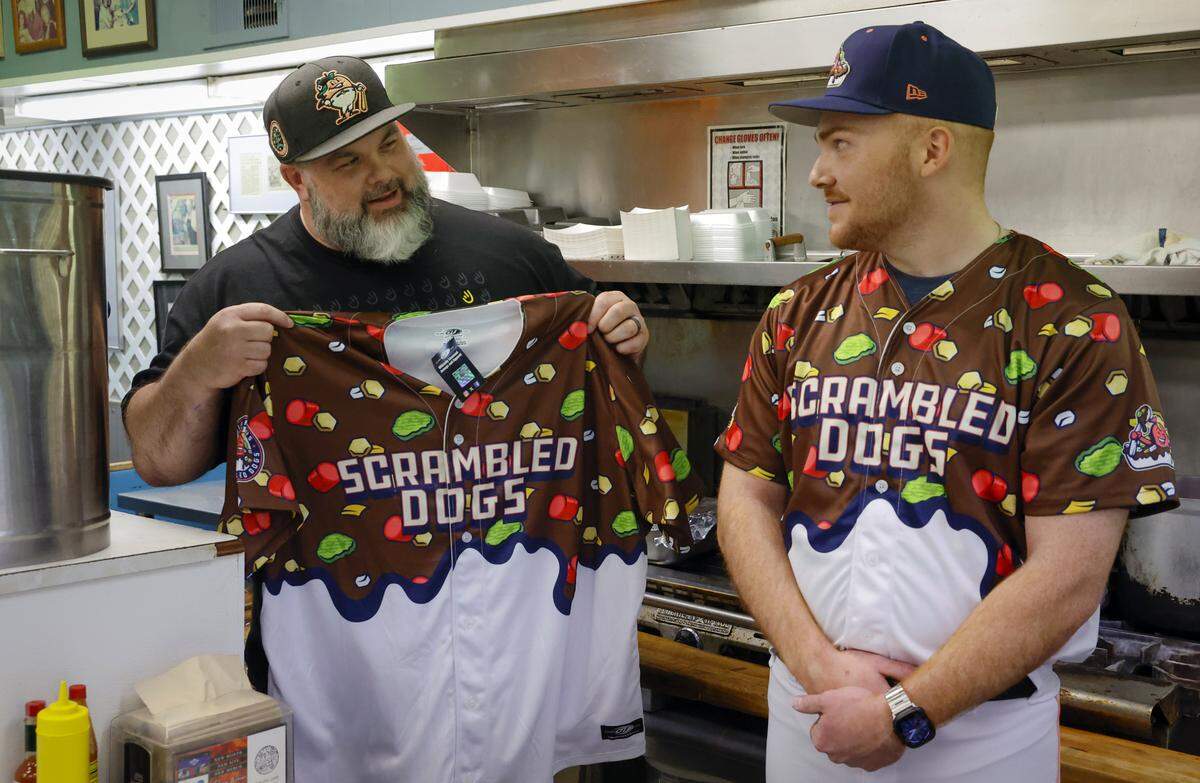 The Columbus Clingstones hosted a news conference April 9, 2026, at Dinglewood Pharmacy in Columbus, announcing “Scrambled Dogs” will be one of the team’s alternate identities. Columbus artist Mike Jones, left, designed the jerseys and associated merchandise for the “Scrambled Dogs” alternate identity.