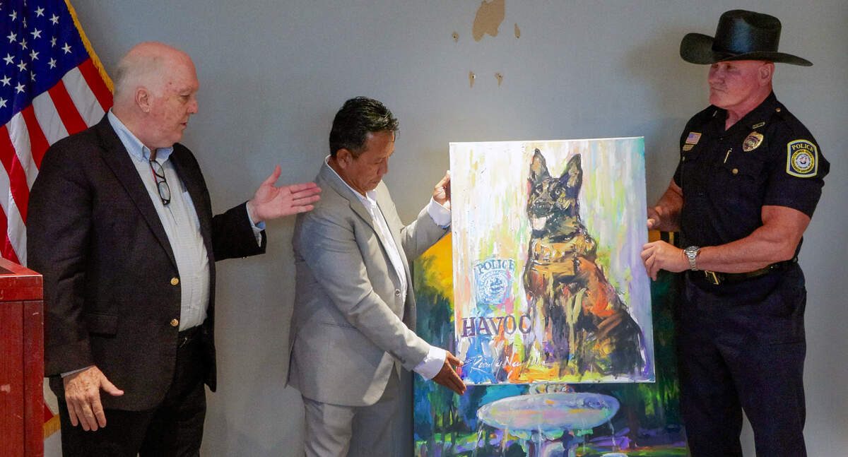 Columbus Police Chief Stoney Mathis, right, accepts a portrait of K9 officer Havoc from Columbus artist Randy Nguyen, center, at a June 29, 2026, news conference in the Public Safety Center as Jed Harris, chairman and co-founder of Back Columbus Blue watches.