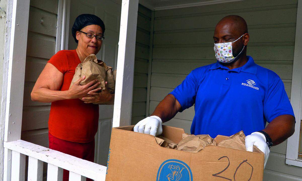 Rodney Close, president and CEO of The Boys & Girls Clubs of the Chattahoochee Valley, gives bags of food to Rita Locke Wednesday afternoon. Although the clubs are closed in the COVID-19 pandemic, but hundreds of Columbus kids still are receiving after-school meals thanks to delivery of food and meals. They are using buses to deliver 300 bags of free meals and snacks Mondays through Thursdays to local youth whose food insecurity is inflamed while the clubs are closed because of the coronavirus, or COVID-19, pandemic.