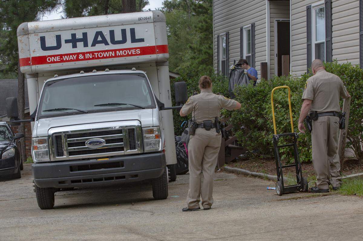 Deputies Hilary Rager and David Podger watch as movers drag garbage bags out of the house on July 20, 2021, in Columbus, Ga. A family member of the evicted drove a U-Haul over after deputies arrived.