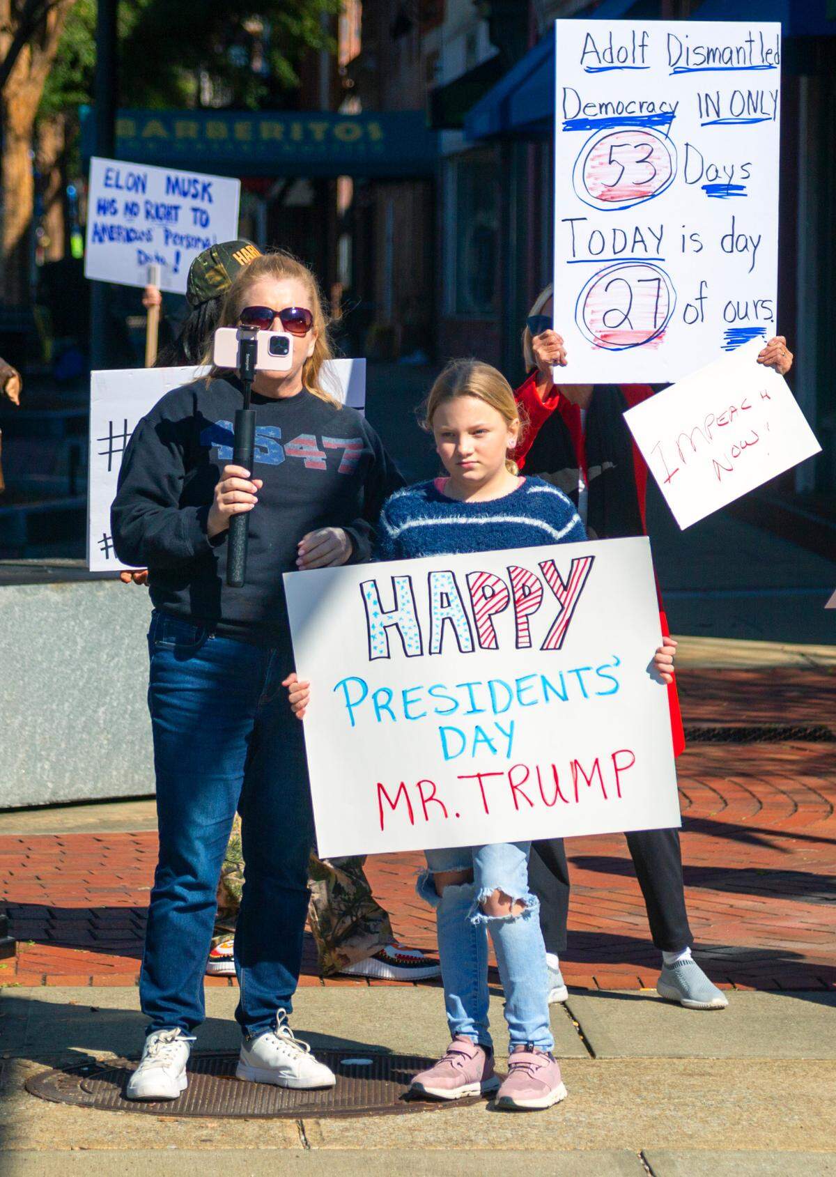 Mary Heisey and her daughter show support of President Donald Trump as people gathered Monday morning at the corner of Broadway and 10th Street in downtown Columbus, Georgia to protest Elon Musk, DOGE, and recent actions by the Trump administration.