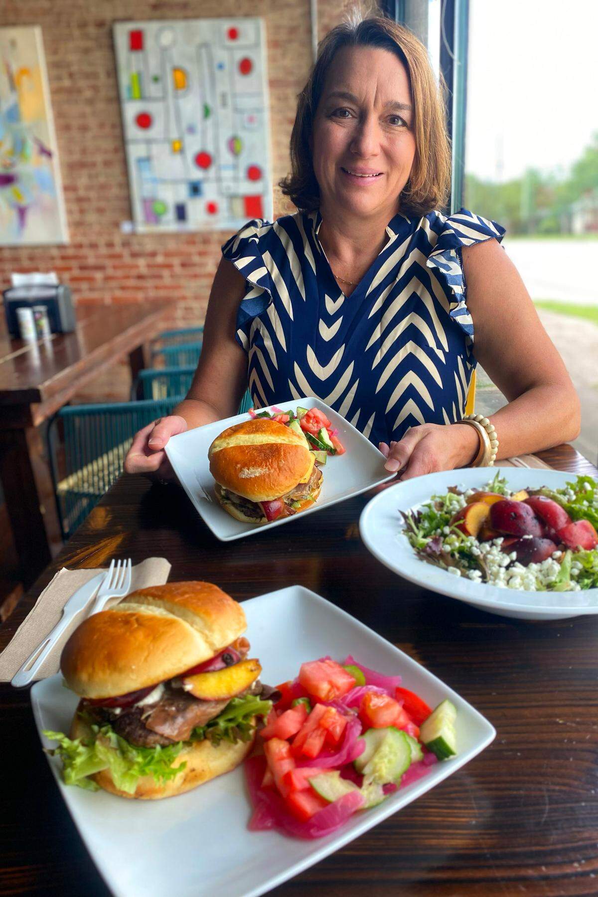 Olivia Amos, owner of The Food Mill in Columbus, shows off The Clingstone Classic Burger, front left. The burger is topped with clingstone peaches and is among the specials The Food Mill is offering this week that include clingstone peaches. 05/28/2025