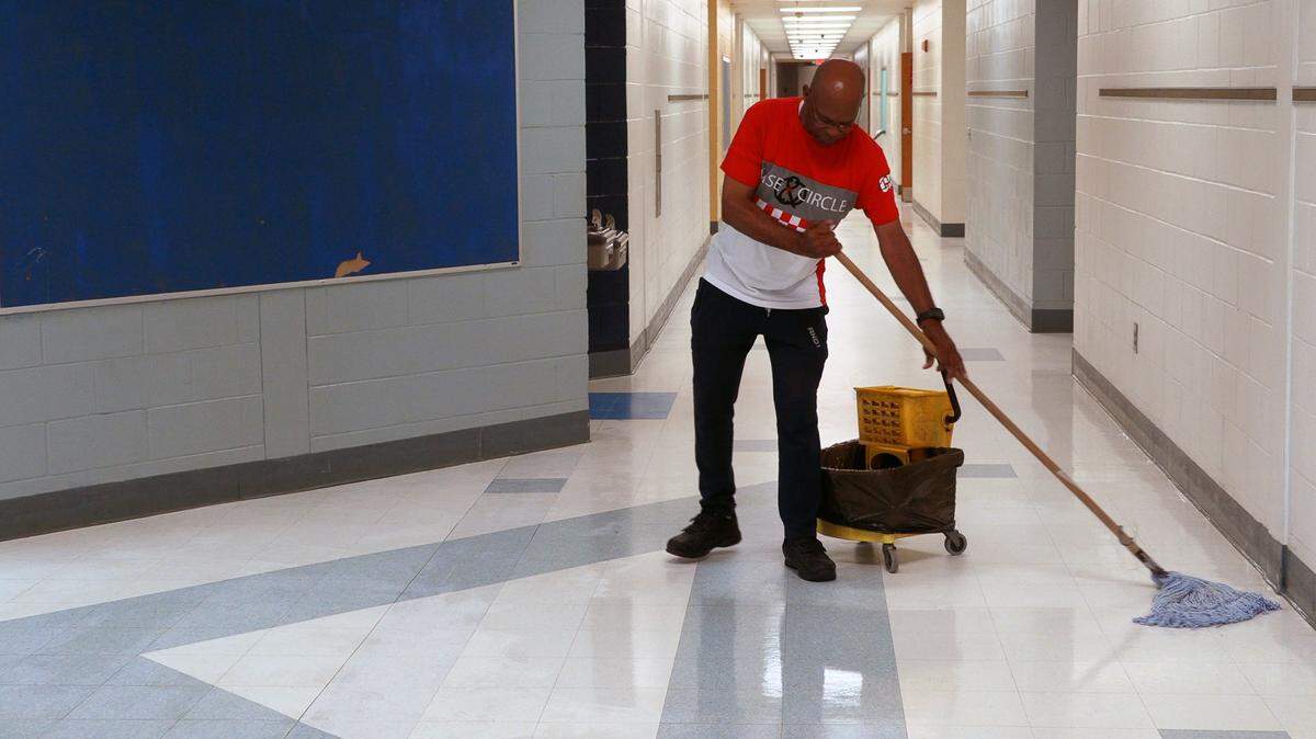 In this June 2019 file photo, Nehemiah Russ, lead custodian at Downtown Elementary Magnet Academy in Columbus, Georgia, applies a coat of wax to a hallway floor.