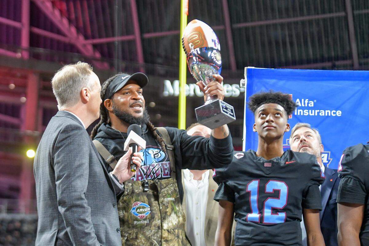 Carver head coach Jarvis Jones raises the trophy as freshman quarterback Sebastian Heard looks up after the Tigers beat Hapeville Charter 24-7 for the Georgia High School Association Class 2A state championship Dec. 16, 2025, at Mercedes-Benz Stadium in Atlanta.