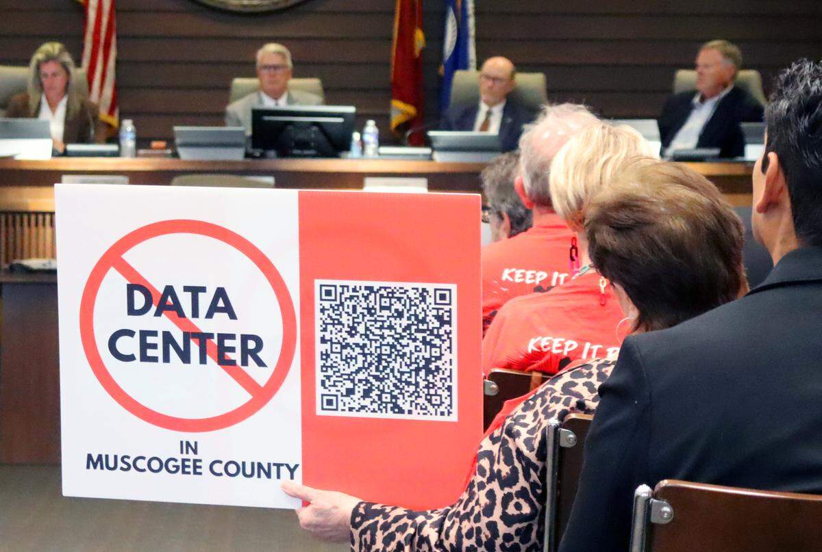 During the June 2, 2026, Columbus Council meeting, a woman holds a “No Data Center” sign with a QR code to a petition against the development of a hyperscale data center in Muscogee County. A sheriff’s deputy escorted her out of the room after she spoke in an outburst from the audience instead of waiting her turn at the podium during the public hearing.