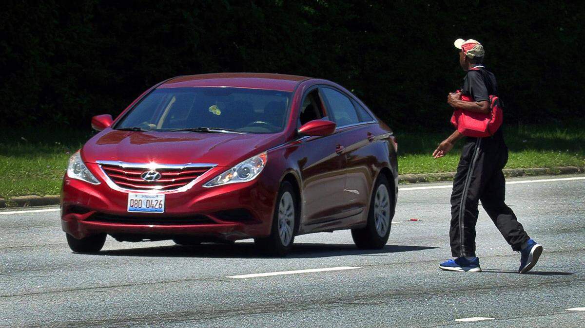 A man crosses Veterans Parkway near 23rd Street, north of the crosswalk at the intersection, as a passing motorist heads south.