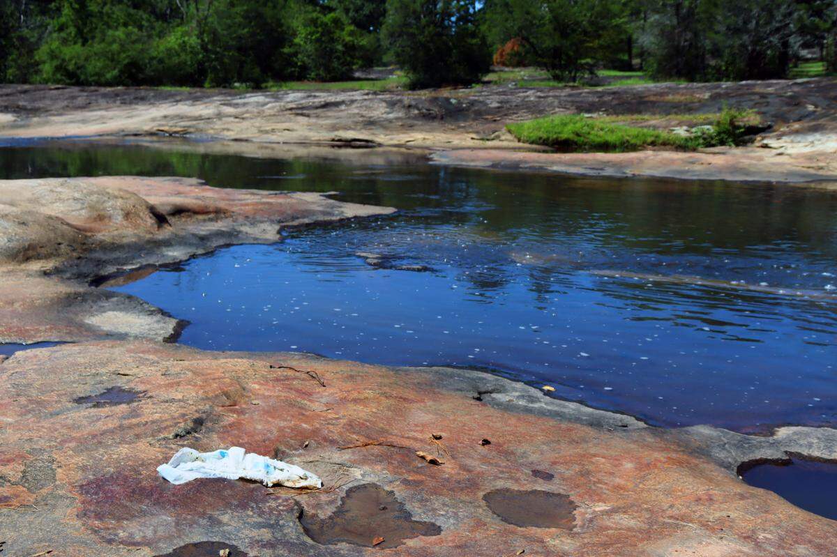 Flat Rock Creek has litter scattered near and in the water. A diaper sits beside the creek before the natural waterslide area. August 2024.