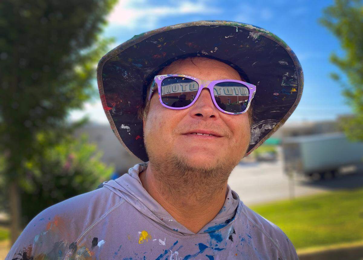 A portion of the mural is reflected in the sunglasses of Chris Johnson, a regional artist painting the new mural on Extra Space Storage at Cross Country Plaza in midtown Columbus on July 14, 2025.