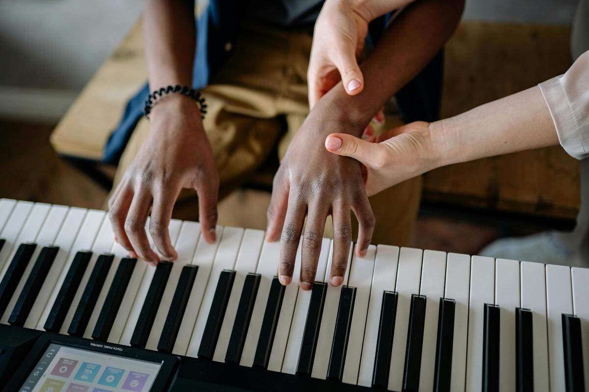 //www.pexels.com/photo/close-up-of-a-person-teaching-a-boy-piano-8520479/
