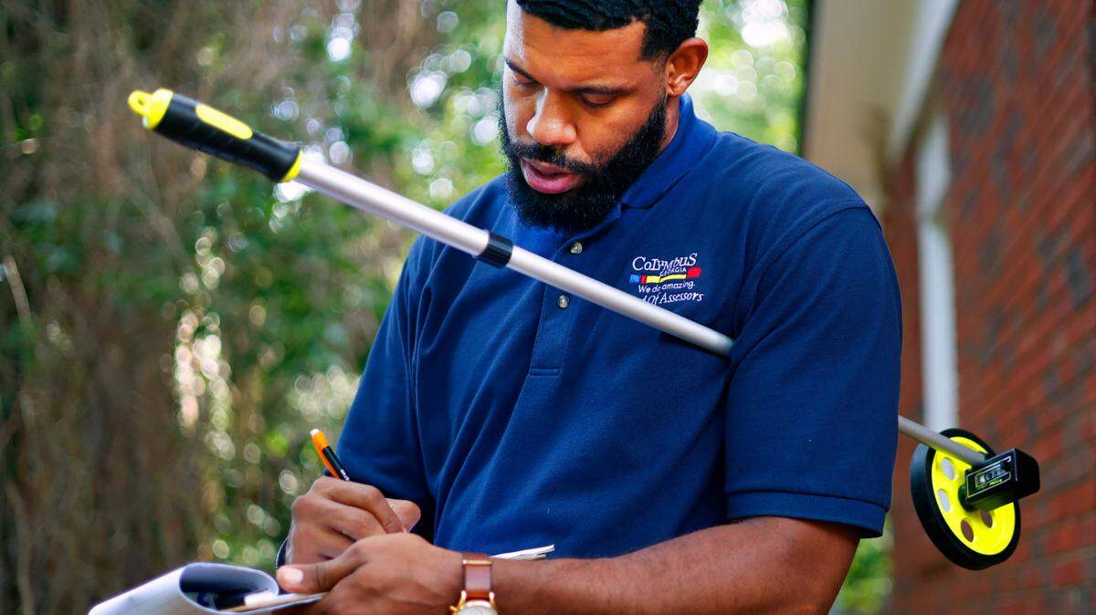 Lorenzo Dowdell Jr., a residential property appraiser with the Columbus Consolidated Government, records measurements he took of the exterior dimensions of a house in Columbus on June 13, 2025.