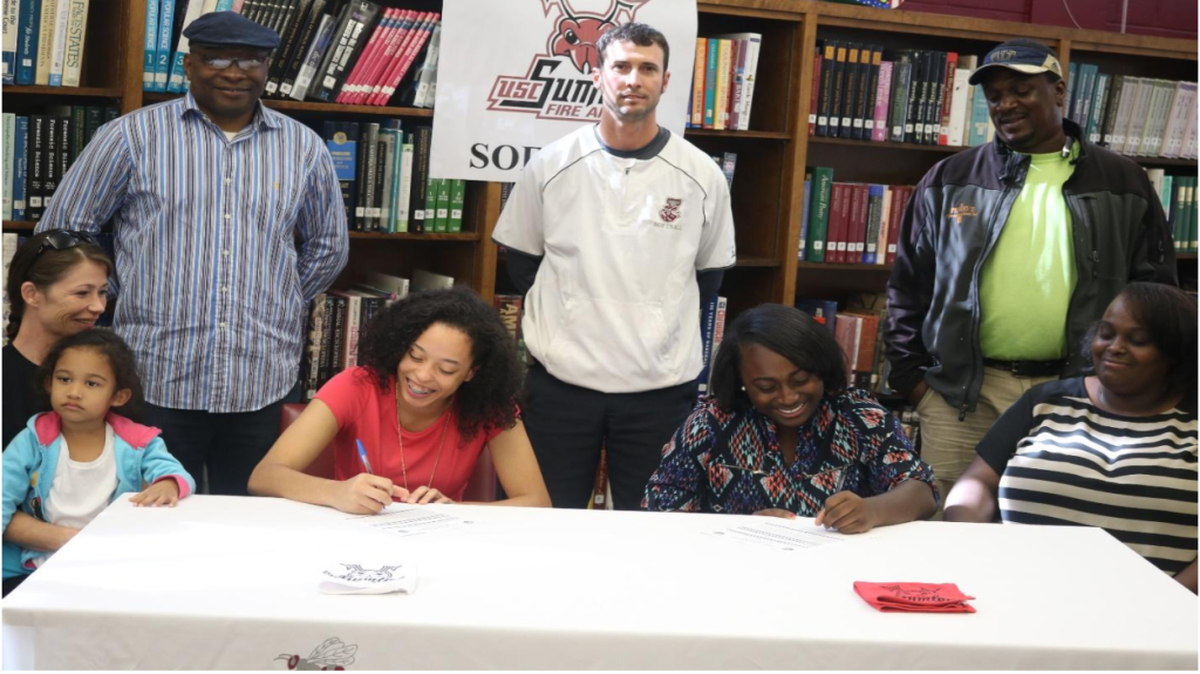 Jordan softball players Jacinda Drayton (left) and Cheyenne Williams (right) sign with USC Sumter while family members and Jordan head coach John Dimitri (back row, middle) watch.