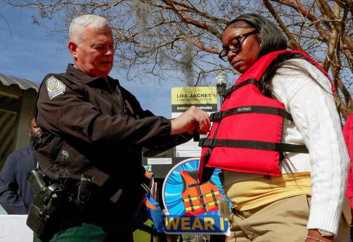 Cpl. Dean Gibson, a game warden with the Georgia Department of Natural Resources, left, discusses the importance of properly securing a life jacket during a news conference March 18, 2026, at Lake Oliver Marina in Columbus, announcing the opening of several life jacket loaner stations across the Chattahoochee Valley.