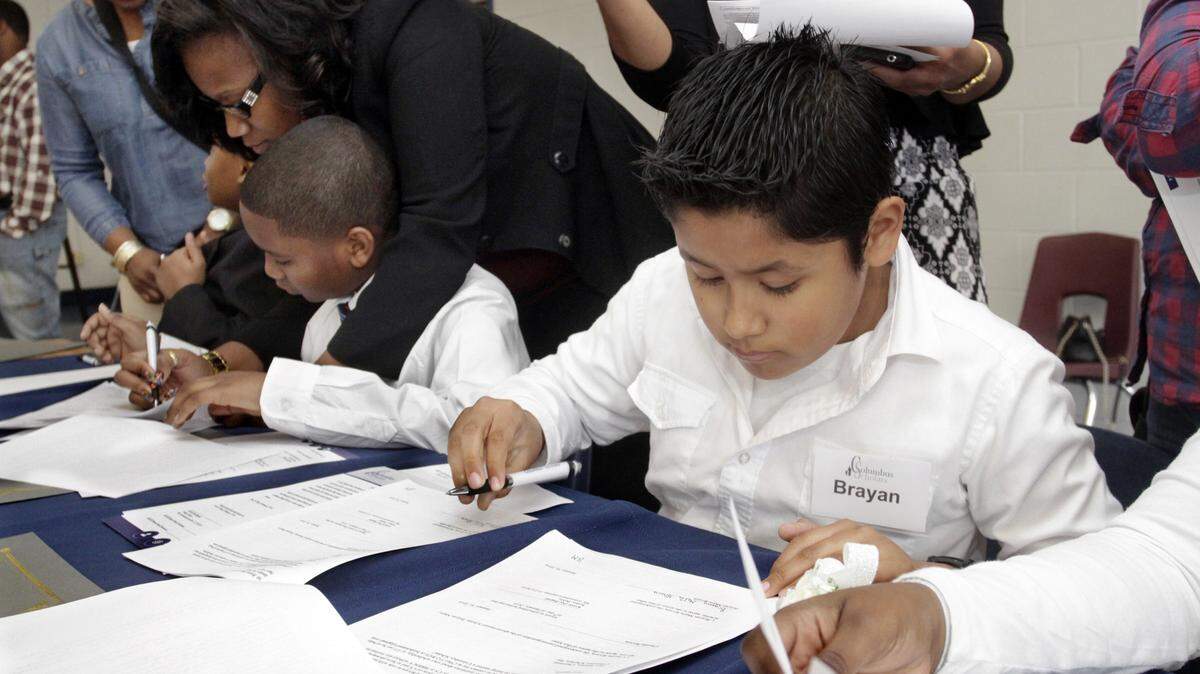 ROBIN TRIMARCHI/rtrimarchi@ledger-enquirer.comBrayan Mejia-Rivera, right, signs his contract with the Columbus Scholars during the seventh annual Columbus Scholars Induction Ceremony at Richards Middle School Saturday. Ten fifth-graders accepted the opportunity to join the program, which provides supplemental funding for their college educations. The students agree to maintain a 3.0 GPA and other behavior guidelines.