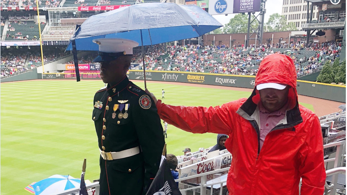 An Atlanta Braves fan shields a member of the Parkview High School JROTC from the rain during a game on Memorial Day 2018
