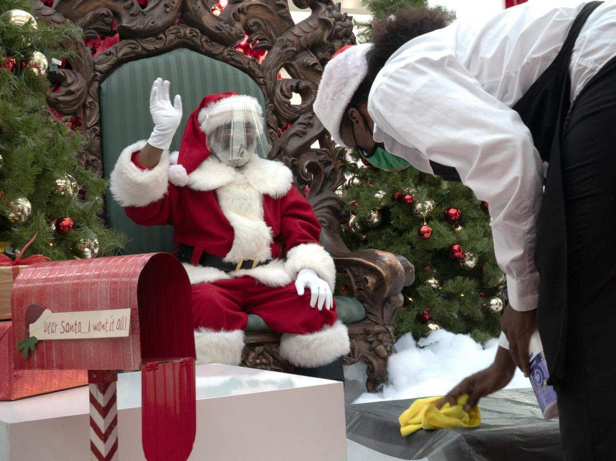 A Cherry Hill Programs employee sanitizes the area where kids sit to greet Santa Claus, wearing a face shield, at the Peachtree Mall in Columbus, Georgia, on Friday, Dec. 18, 2020.