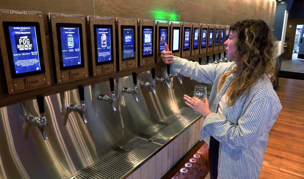 Sarah Algoe, marketing director for the Uptown Life Group, demonstrates the self-serve beer wall and wine delivery system at The Mix Market, located at 1040 Broadway in downtown Columbus, Georgia. 09/19/2023