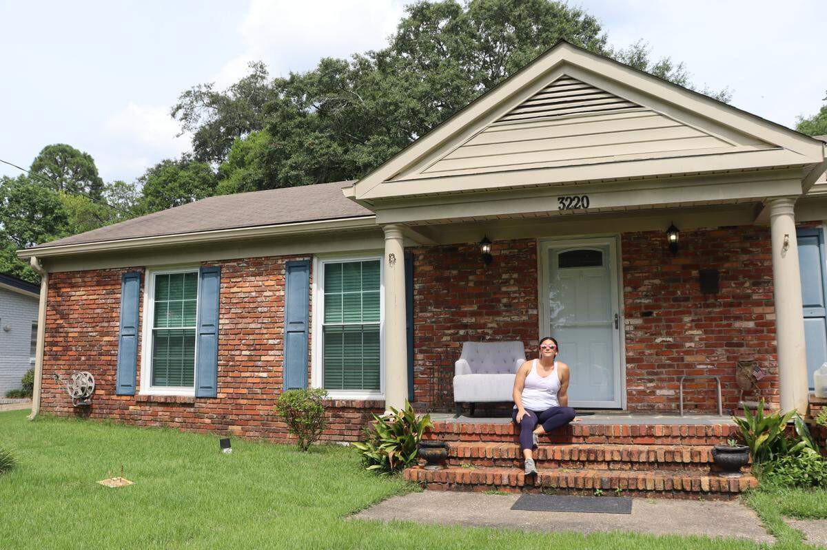 Kat Cannella sits in front of her home in Mohina Woods in July 2024. Her home was 81 degrees. The “cool room” was 70 degrees. She’s never had a bill higher than $300 in her 12 years at this home.