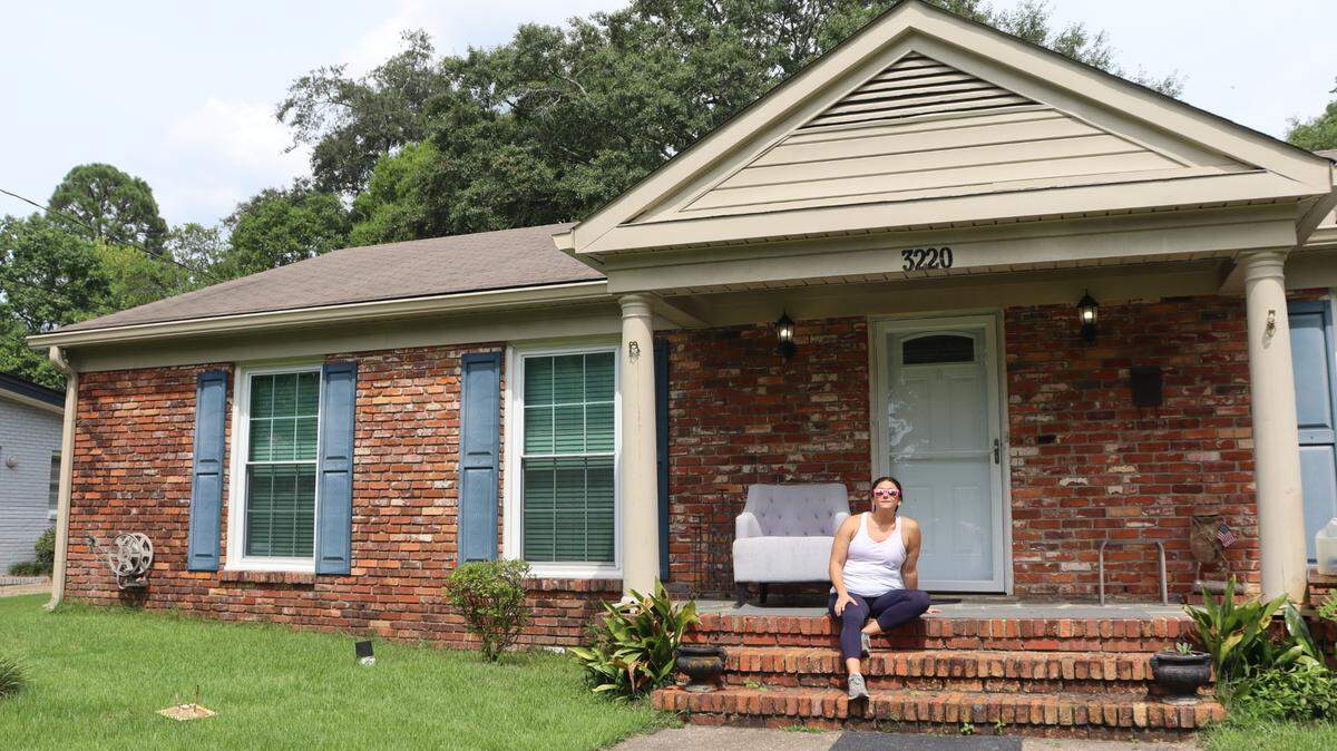 Kat Cannella sits in front of her home in Mohina Woods in July 2024. Her home was 81 degrees. The “cool room” was 70 degrees. She’s never had a bill higher than $300 in her 12 years at this home.