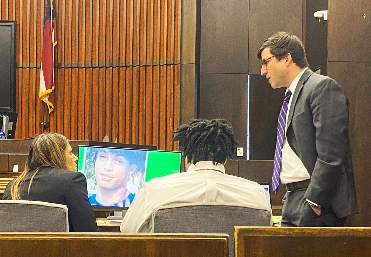 Left to right, attorney Sirena Saunders, defendant Emmanuel Truitt and attorney Bentley Adams IV confer as a photo of victim Dondre Reynolds appears on a computer screen.