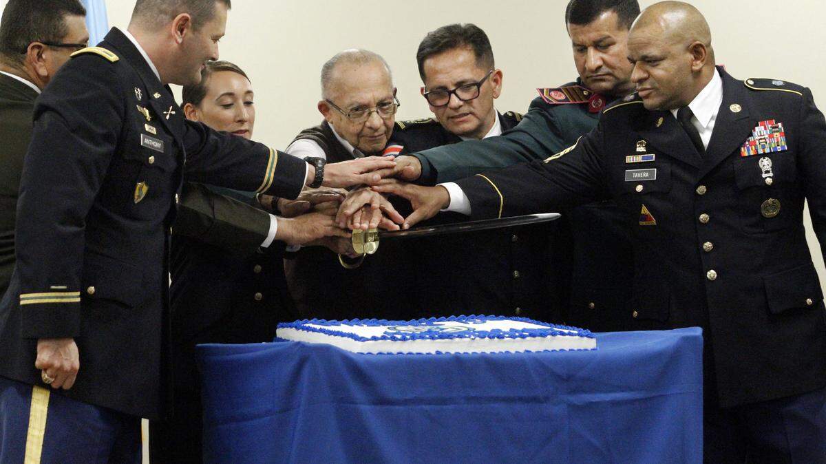 FILE -- Military officials with the Western Hemisphere Institute for Security Cooperation place their hands on a saber to cut the cake commemorating the Institute's 15th anniversary on Jan. 14, 2016. From left: U.S. Army Col. Keith Anthony, WHINSEC commandant; Col. Luis Viera of El Salvador, WHINSEC assistant commandant; U.S Army 1st Lt. Sophia Navedo, the youngest WHINSEC instructor; Mauricio Lawson, the oldest WHINSEC employee; Col. Walter Navarro of Costa Rica; Command Sgt. Maj. Digno Galeano of Paraguay, WHINSEC guest command sergeant major; and U.S. Army Command Sgt. Maj. Abel Tavera, WHINSEC command sergeant major.