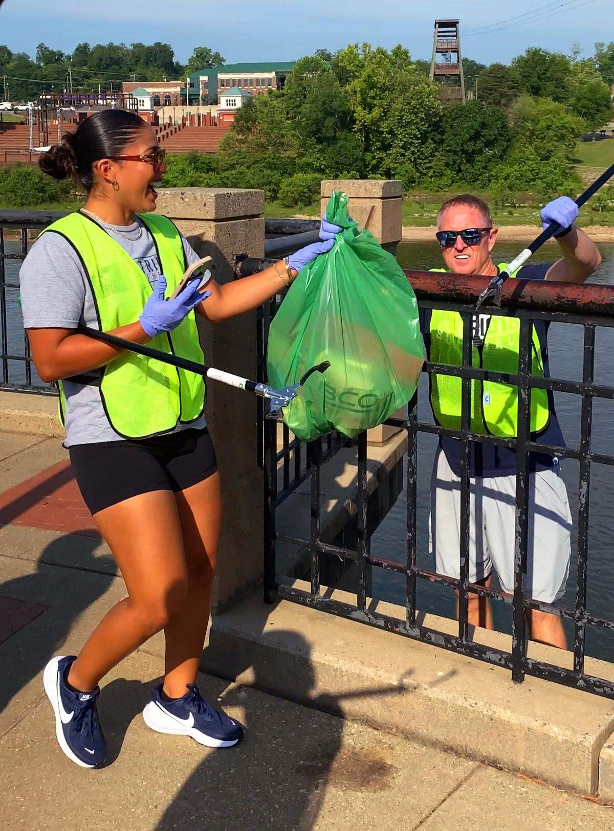 University of the Cumberlands head softball coach Bruce Lenington, right, said service is a big part of the NAIA’s mission and a way to give back to host communities. College softball players in Columbus for the 2026 NAIA Softball World Series swapped their softball gloves for disposable gloves May 20, 2026, to beautify the Chattahoochee Riverwalk. Players and coaches from two schools, the University of the Cumberlands in Williamsburg, Kentucky, and Marian University in Indianapolis scoured the Riverwalk for trash, debris and litter as part of the Champions of Character Cleanup effort organized by the Keep Columbus Beautiful Commission and the Columbus Sports Council.