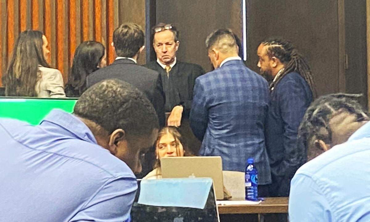 Terrance Upshaw, left in the foreground, whispers to codefendant Rodderick Glanton as Judge Gil McBride holds a bench conference with attorneys in the background.