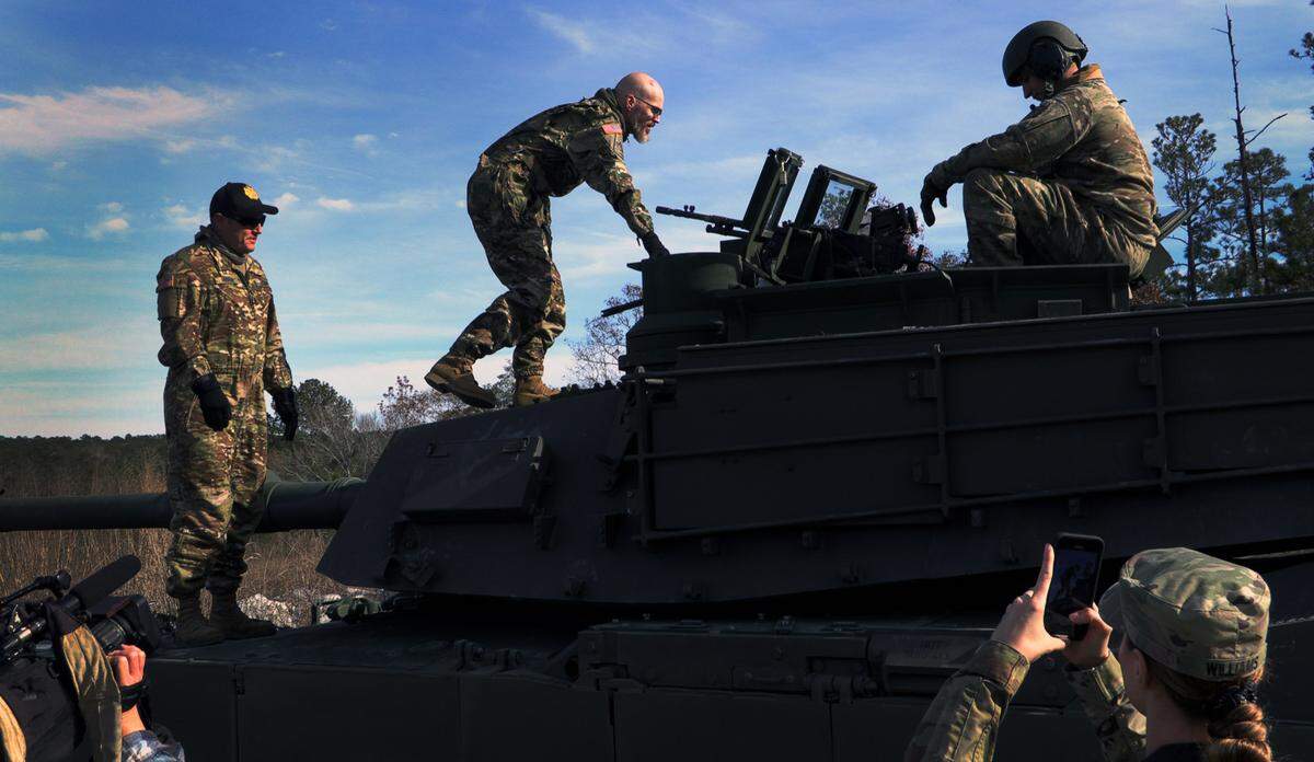 Jay Tenison, a military veteran currently fighting Stage IV stomach cancer, center, climbs onto a tank Tuesday afternoon at Fort Moore, Georgia. 12/05/2023