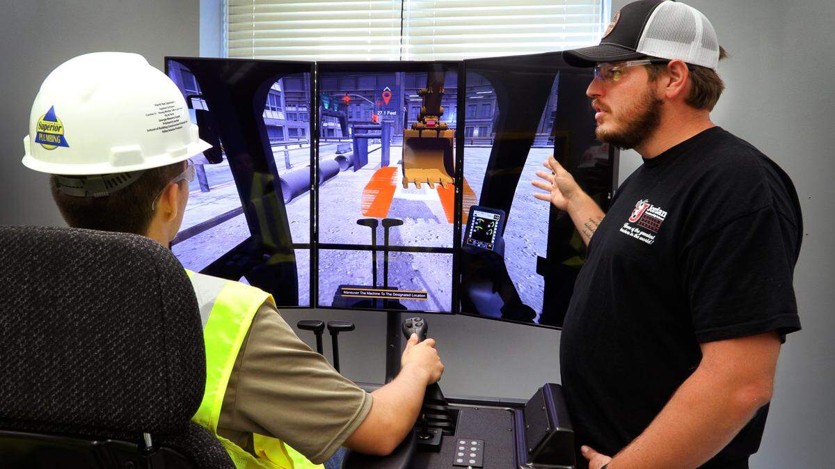 Jimmy Napier, right, a teacher at Jordan Vocational High School, and Kevin Hunt, 17, a junior at the school, demonstrate one of the CAT Simulators that’s part of the school’s Heavy Equipment Operator Training Program. 09/23/2022