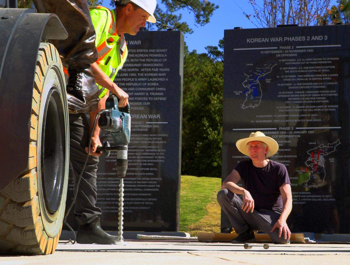 Sculptor Jay Warren, right, supervises as a worker prepares to drill a hole for the of a larger-than-life statue of Col. Ralph Puckett Jr. to the Korean War Memorial at the National Infantry Museum. 10/21/2024