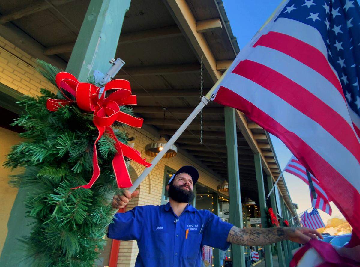 Devan Bolton,a maintenance worker for the city of Plains, Georgia, hangs flags in downtown Plains Monday morning. 12/30/2024