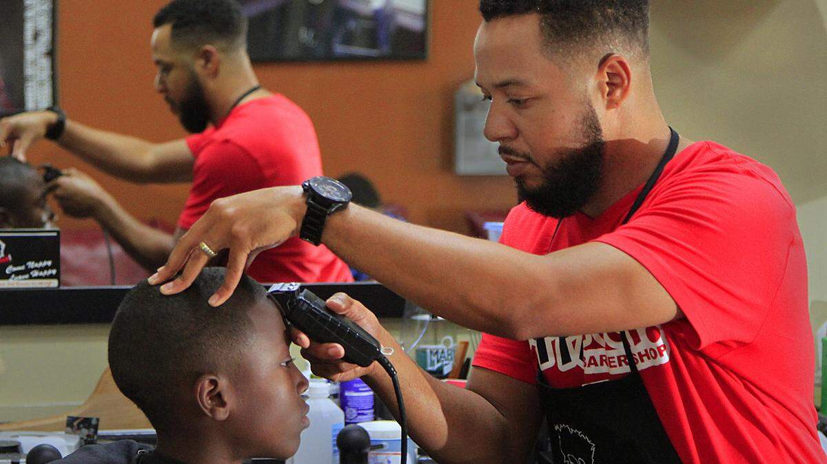 Mike Haskey/mhaskey@ledger-enquirer.comBrandon Hicks, owner of The Nappy Root Barber Shop on Macon Road, gives a haircut to Keyon Burns,10. Aug. 21.