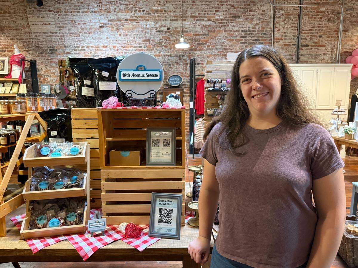 Kristin Everett, owner of 18th Avenue Sweets, poses next to her display booth inside The 706 Social, 1025 Broadway in Columbus.