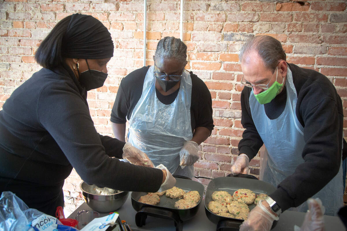 Instructor Tiffany Dunn helps participants Vanessa Knowles and Hal Campbell cook chicken burgers at The Food Mill in Columbus, Ga. on March 14, 2022.