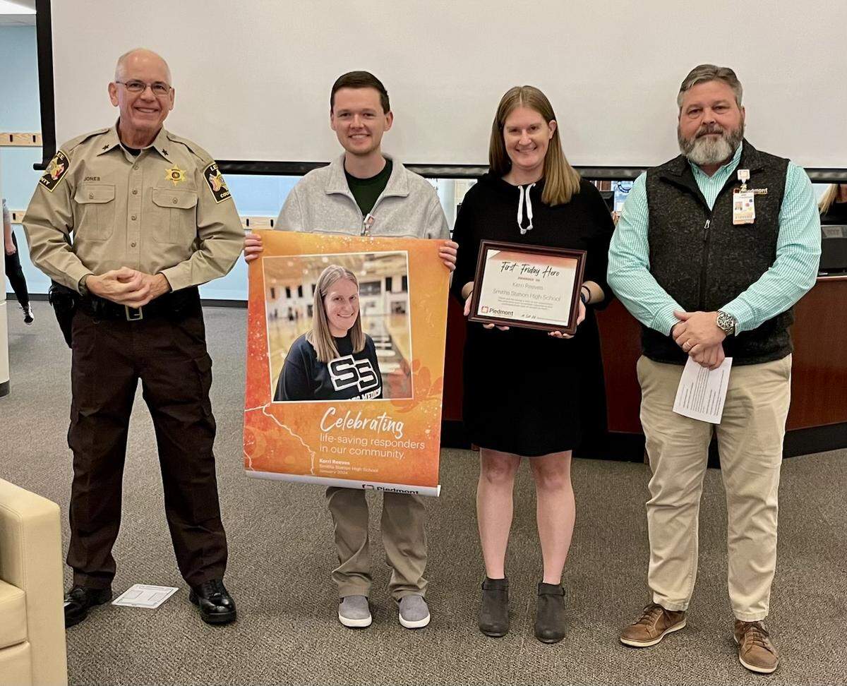 From left, Lee County Sheriff Jay Jones, Piedmont Columbus Regional senior communications specialist John “JT” Fellows, Smiths Station High School athletics trainer Kerri Reeves,and Piedmont Columbus Regional public safety director Mike Brown pose for a photo Jan. 5, 2024, at the school. Reeves, employed by the Hughston Clinic in Columbus, is the Piedmont Columbus Regional First Friday Hero for January after her actions convinced a 16-year-old gunman to back off his threat to kill another student following their fight in the SSHS gym during basketball practice Nov. 2, 2023.