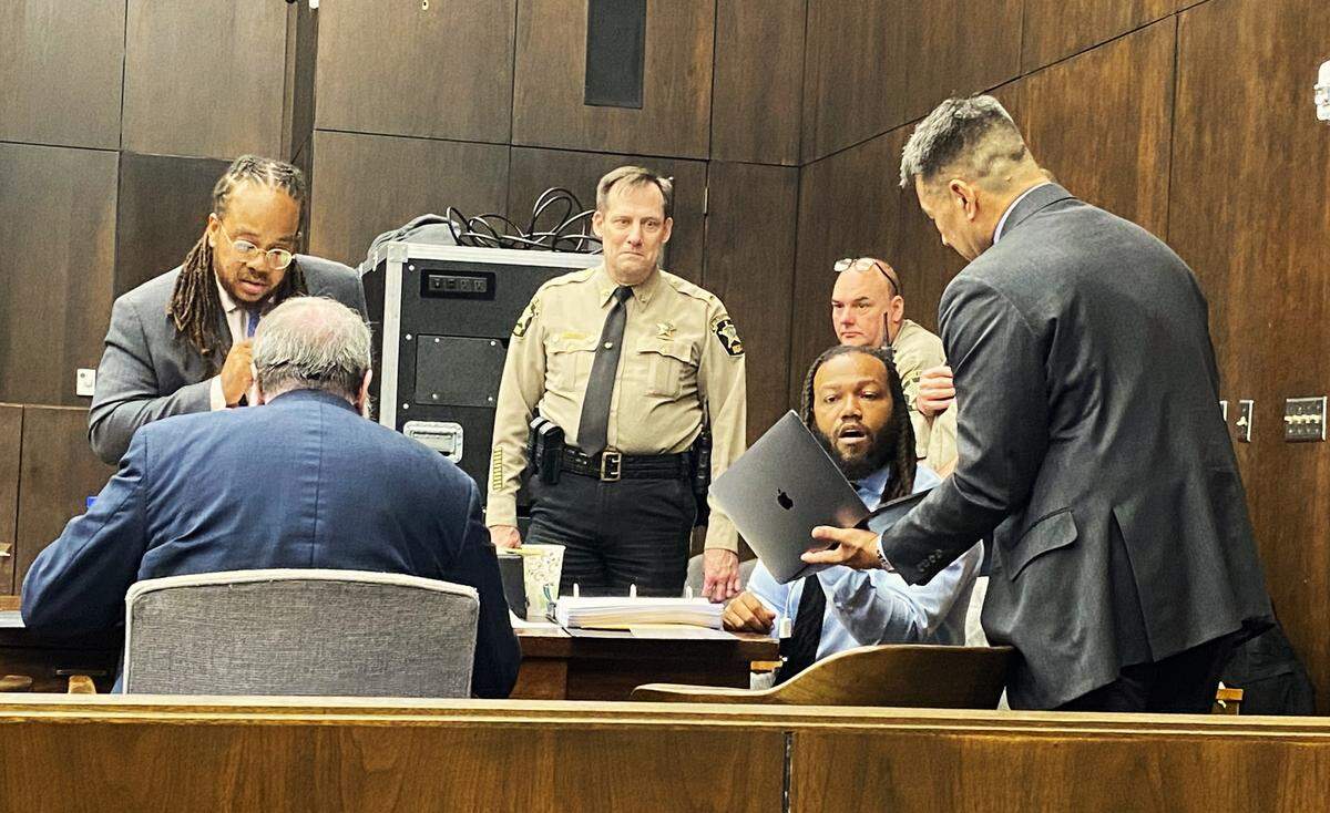 Sheriff’s deputies watch as the defense attorneys talk before jury selection Monday.