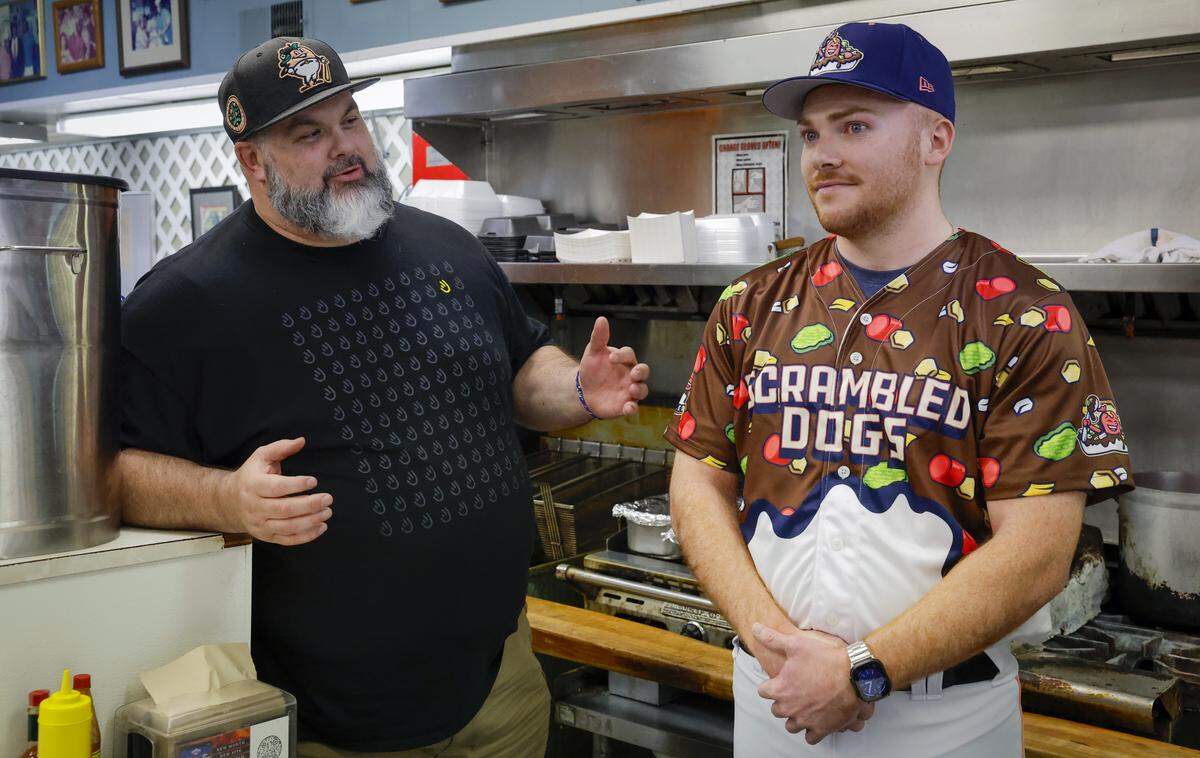 The Columbus Clingstones hosted a news conference April 9, 2026, at Dinglewood Pharmacy in Columbus, announcing "Scrambled Dogs" will be one of the team's alternate identities. Columbus artist Mike Jones, left, designed the jerseys and associated merchandise for the “Scrambled Dogs” alternate identity.