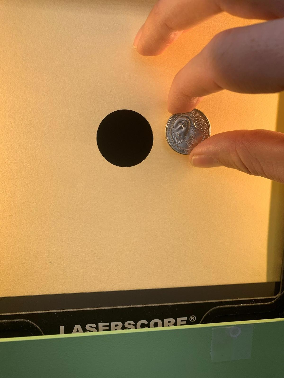 Sgt. Ivan Roe holds up a quarter to show the size of the target in the 10 meter air rifle event. The black dot shown encompasses scoring rings four through 10 in this event.