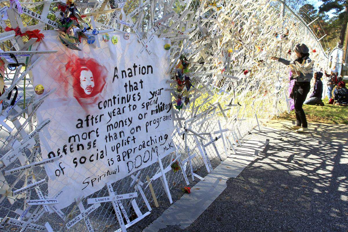 Demonstrators place crosses onto a fence separating them from Fort Benning property during the SOA Watch protest Nov. 22, 2015.