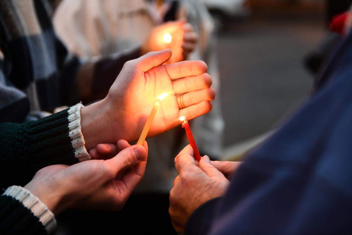 Attendees of a menorah lighting ceremony on Nov. 28, 2021 in downtown Columbus help each other light candles during the program.