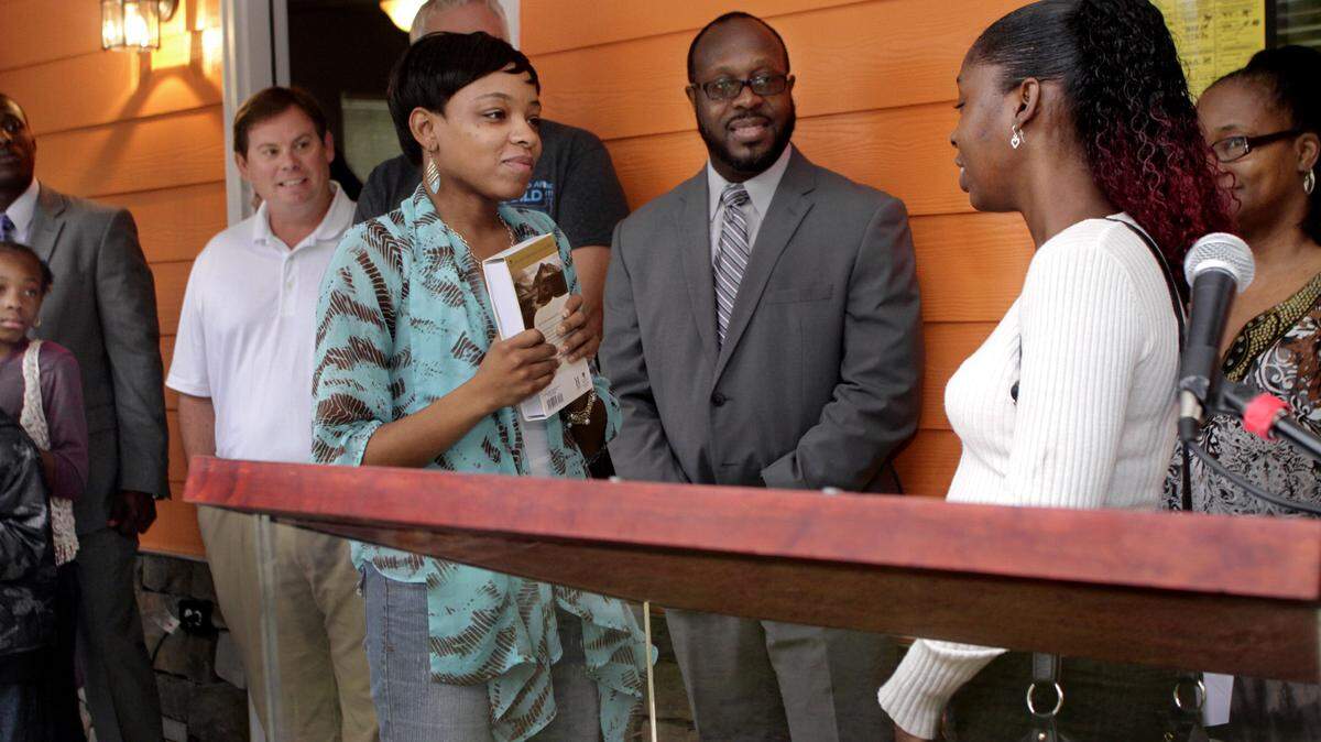 Tyra Alexander, center left, listens as Deandra Taylor, a recent Habitat for Humanity homeowner, congratulates her and hands her the keys to her new home on 42nd Street. Alexander is holding a Bible presented to her by Brenda Crawford, far right, also a recent Habitat for Humanity homeowner.
