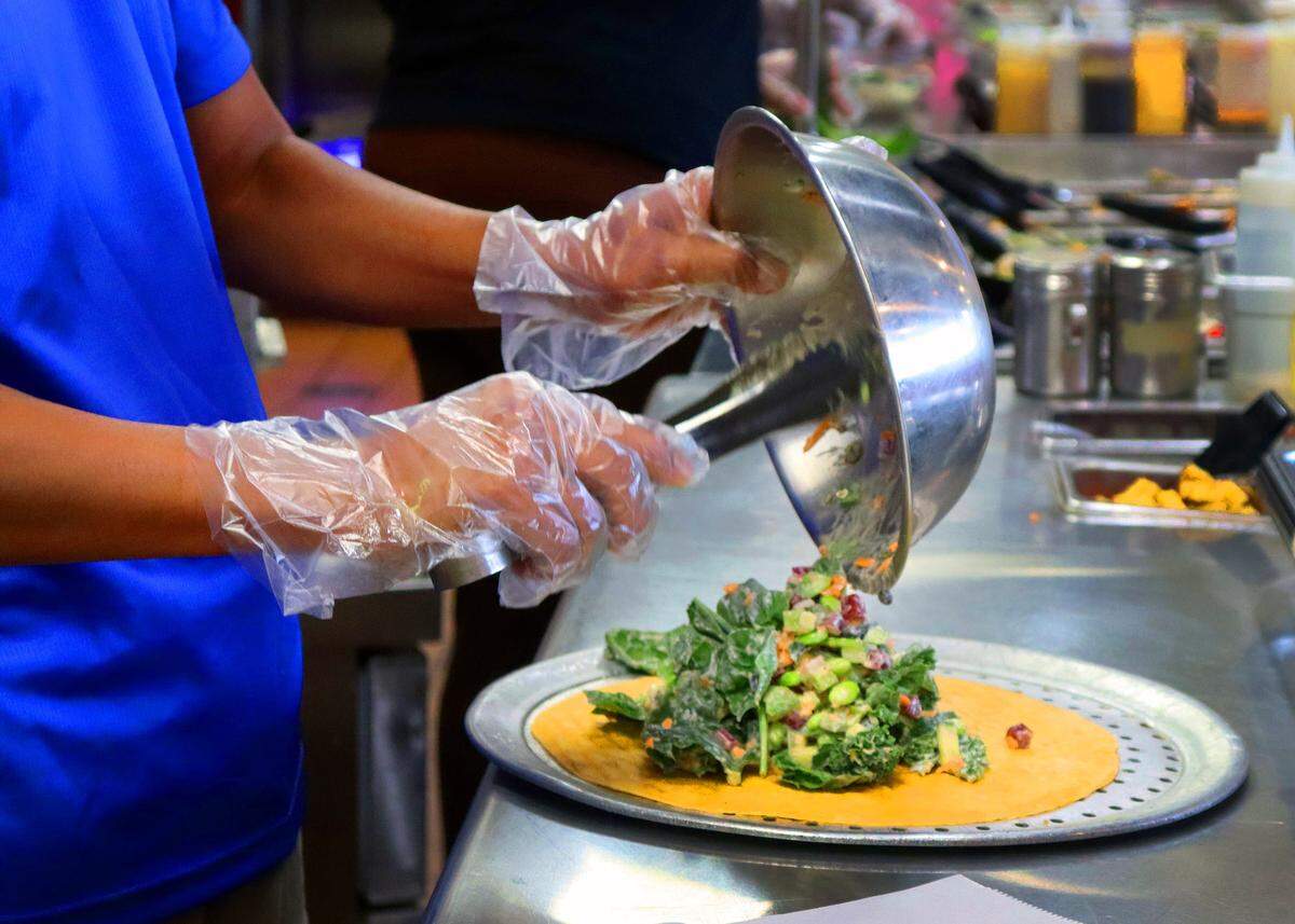 Hati Budiyono, co-owner of Build Yo Salad builds a vegan salad with avocado for under $11.