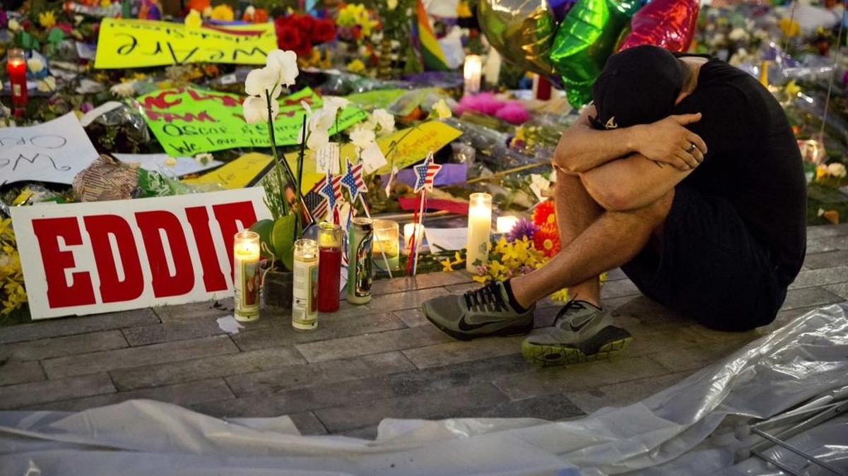 Jean Dasilva sits next to a makeshift memorial for the victims of Sunday's mass shooting at the Pulse Orlando nightclub as he mourns the loss of his friend Javier Jorge-Reyes Tuesday in Orlando, Fla.