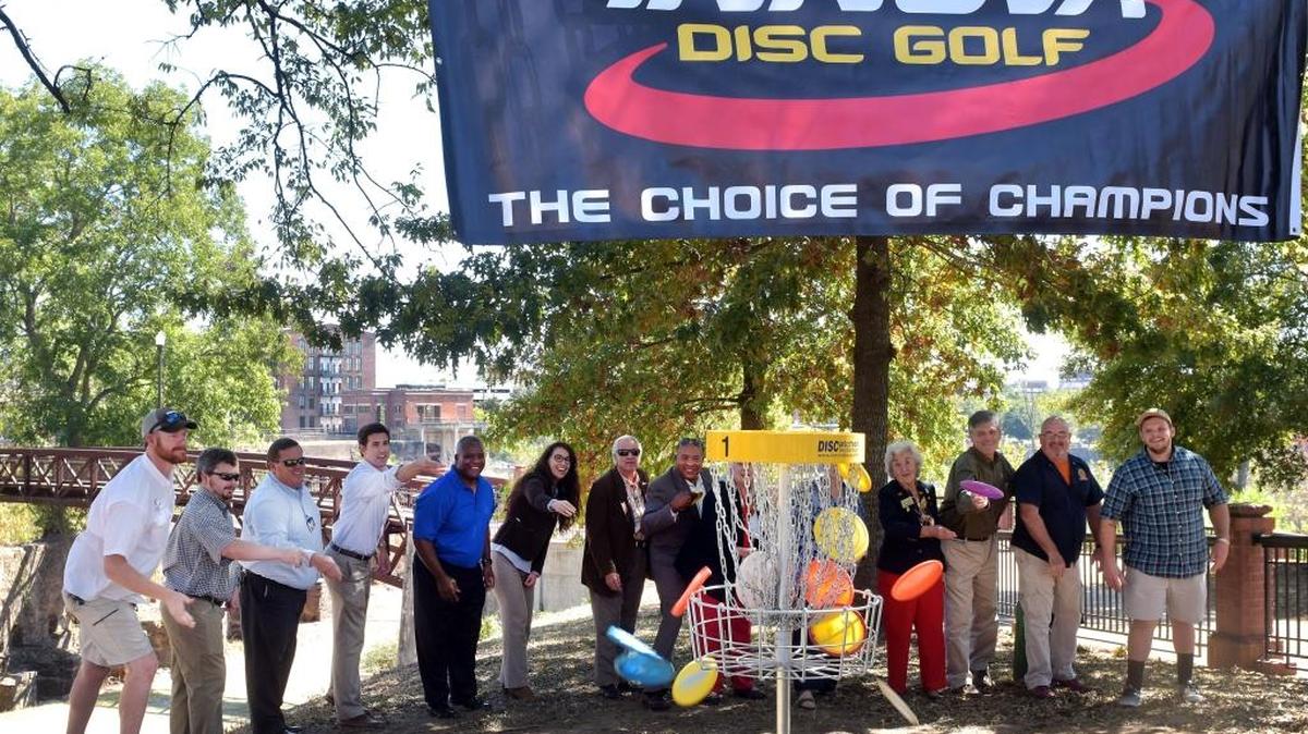 Phenix City and White Water Express officials cutting the virtual ribbon for the Phenix City Disc Golf by throwing Golf Disks at the 1st Golf Basket along the Phenix City riverfront Wednesday afternoon October 12, 2016