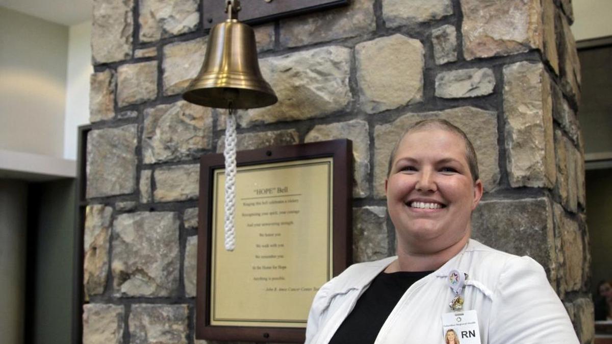 Shondra Nelson is a thoracic oncology nurse navigator at the John B. Amos Cancer Center. Nelson, who is also a cervical and lung cancer survivor, guides patients through the process of treatment and recovery. She is standing in front of the “Hope” bell in the center’s lobby that patients ring after completing treatment.