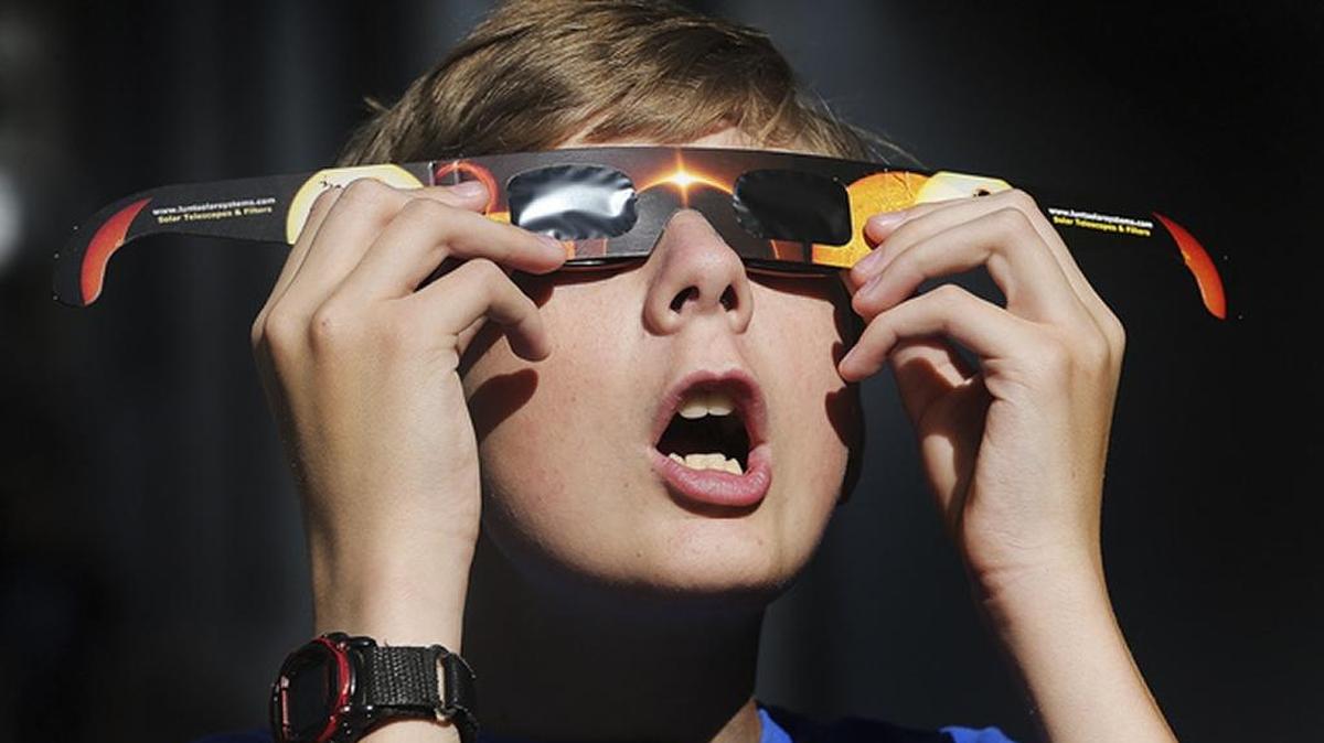In this Wednesday, Aug. 16, 2017 photo, Colton Hammer tries out his new eclipse glasses he just bought from the Clark Planetarium in Salt Lake City in preparation for the Aug. 21 eclipse. Eye doctors urge strict adult supervision for eclipse watchers under 16 years old.